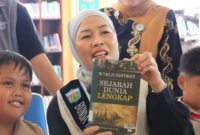 Bunda Literasi Kota Sungai Penuh, Sri Kartini Alfin, S.Kep., Ns, saat berada di perpustakaan dan menujnjukkan buku.(poto: istimewa).