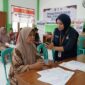 Petugas Agen Perlinsos mendampingi warga melakukan verifikasi wajah pendaftaran bansos 2027 di kantor kelurahan.(ilustrasi poto: AI).