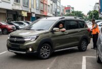 Pengemudi mobil bermanuver perlahan dibantu juru parkir saat parkir di ruang sempit area perkotaan padat.(poto: AI).